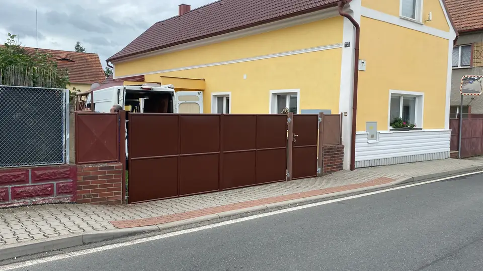 Hnědý plechový plot a branka podél ulice